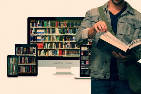 Student przeglądający książkę na tle komputera i tabletów