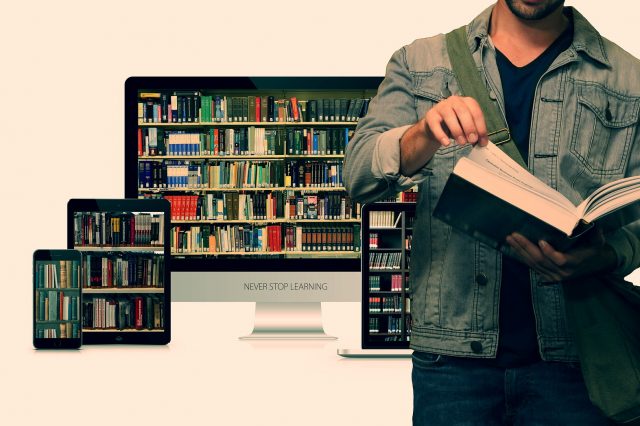 Student przeglądający książkę na tle komputera i tabletów