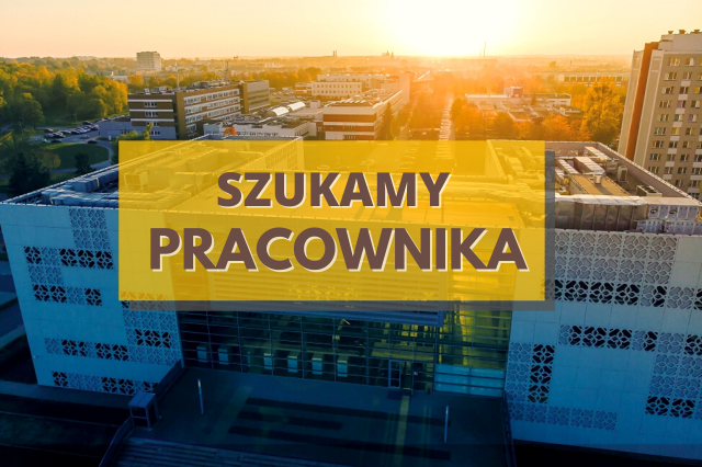 Brązowy napis: "Szukamy pracownika" na żółtym tle. Za nim budynek biblioteki i kampus PB.