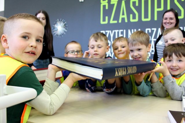Uśmiechnięte dzieci trzymające w ręku dużą księgę.
