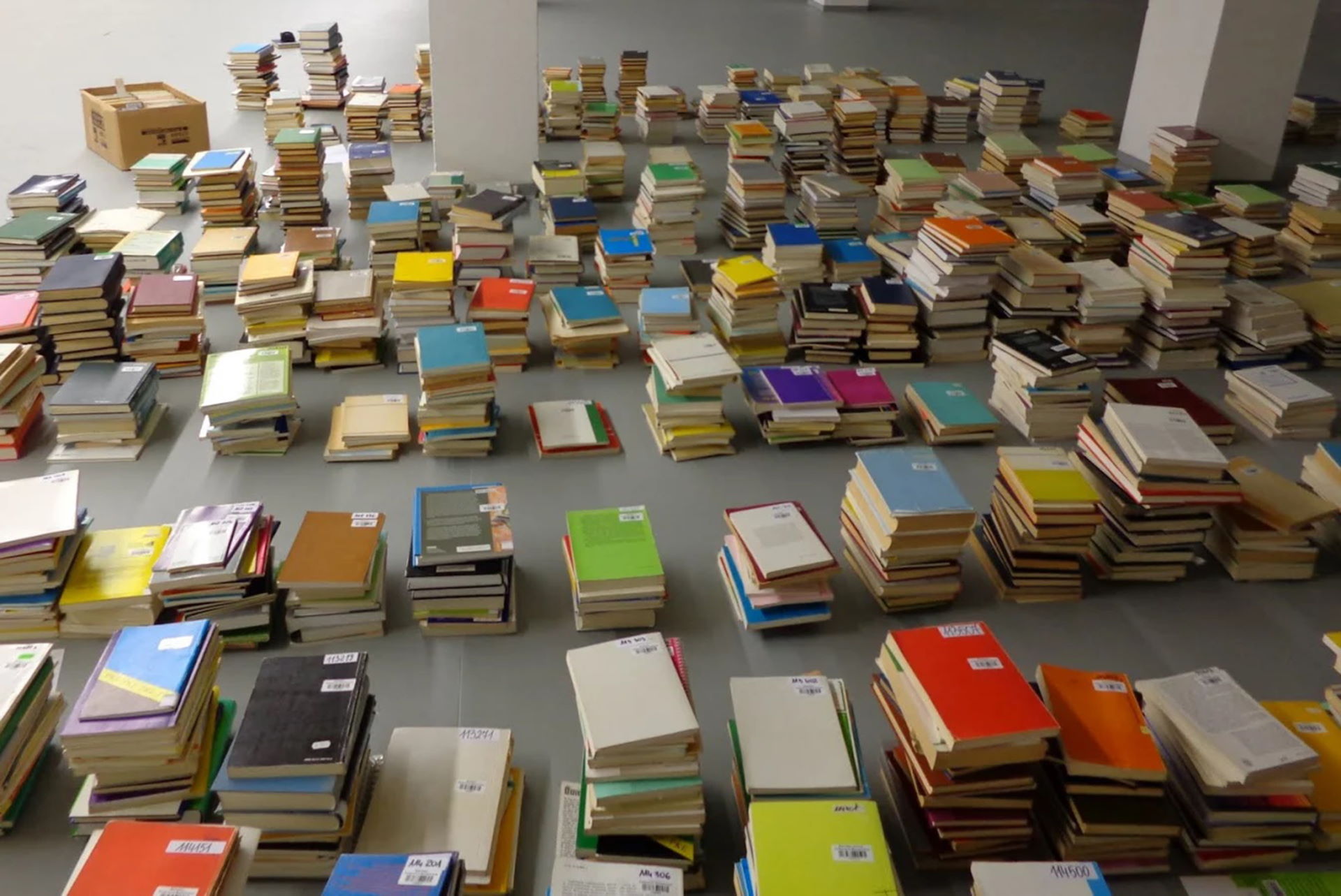 Szara podłoga na której leżą książki poukładane w stosy po kilka lub kilkanaście sztuk.