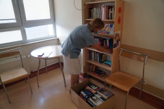 Kobieta w masce rozkładająca książki na regale. Przed nią karton z książkami.