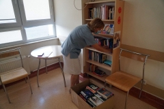 Kobieta w masce rozkładająca książki na regale. Przed nią karton z książkami.