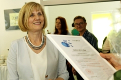 Zbliżenie na uśmiechniętą dyrektor biblioteki Marię Czyżewską. Z prawej strony widać kartę papieru z tekstem w białej ramce.