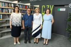 Cztery stojące obok siebie osoby na tle regałów z książkami. Od lewej: kobieta z ciemnymi włosami w kwiecistej bluzce,  mężczyzna w okularach i ciemnej koszuli, Dyrektor Biblioteki PB oraz Zastępca Dyrektora.
