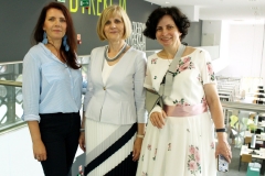Trzy stojące obok siebie kobiety. Od lewej: kobieta z ciemnymi włosami, blondynka w jasnym żakiecie  i spódnicy oraz brunetka z włosami do ramion, w jasnej kwiecistej sukience, z prawą ręką na temblaku.