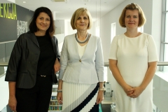 Trzy stojące obok siebie uśmiechnięte kobiety. Od lewej: kobieta z ciemnymi włosami, blondynka w jasnym żakiecie  i spódnicy oraz blondynka w białej j sukience.