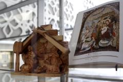 Z lewej strony drewniana szopka z Jezusem w żłóbku, Maryją i Józefem, z prawej książka z ikoną ukazującą Trzech Króli składających pokłon przed Świętą Rodziną.