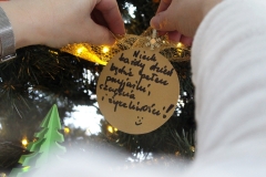 Ręce wieszające na choince papierową, złotą bombkę z życzeniami: Niech każdy dzień będzie pełen przyjaźni, szczęścia i życzliwości!