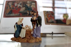 Figurka ceramiczna ukazująca Jezusa w żłóbku, Maryję i Józefa. W tle książka z ikonami.