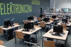 Stoliki z komputerami do pracy dla czytelników Czytelni Elektronicznej. W tle zielony napis na ścianie.