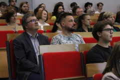 Grupa osób siedzących na krzesłach stacjonarnych. W centralnym punkcie zdjęcia trzech mężczyzn.