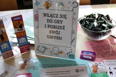 Zbliżenie na stół, na którym znajdują się kolorowe broszury oraz gadżety promocyjne.