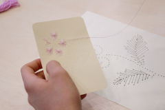 Zbliżenie na dłoń trzymającą kartonik z wyhaftowanym różowym kwiatkiem