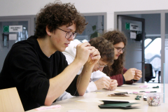 Uczestnicy przy stole wyszywają wzory na kartonikach