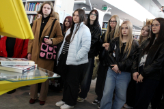 Grupa dziewczyn stoi wokół żółtego interaktywnego stanowiska (kiosku) bibliotecznego, z uwagą wpatrując się w ekran