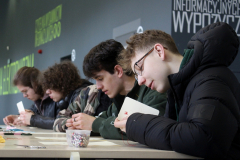 Profil kilku chłopaków  wspólnie zajmujących się haftem, siedzących z uwagą przy dużym wspólnym białym stole