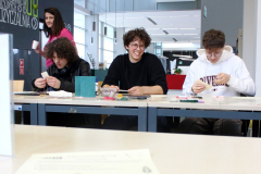 Uczestnicy wyszywają kartki przy stole w bibliotece