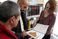 Bibliotekarka pokazuje dwóm mężczyznom książkę w języku Braille’a z rysunkiem cerkwi. W tle regał z książkami.