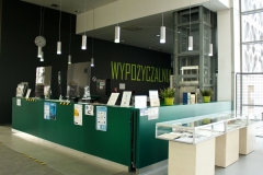 Zielona lada wypożyczalni Biblioteki PB, w tle szara ściana z zielonym napisem.