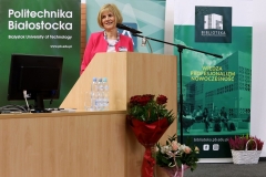 Przy mównicy stoi Dyrektor Biblioteki Politechniki Białostockiej Maria Czyżewska. Uśmiecha się do słuchaczy.