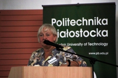 Kobieta o krótkich jasnych włosach we wzorzystym beżowo-szarym żakiecie przemawia z mównicy. W tle baner z napisem: Politechnika Białostocka.