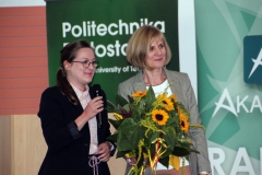 Dwie uśmiechnięte kobiety stoją obok siebie, z prawej dyrektor Biblioteki PB Maria Czyżewska, trzymająca kwiaty, z lewej kobieta trzymająca  mikrofon.