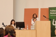 Aula. Dwie kobiety zwrócone przodem do słuchaczy. Kobieta po prawej jest w białej bluzce. Druga kobieta siedzi za monitorem.