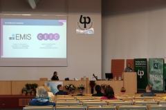 Aula. Dwie kobiety zwrócone przodem do słuchaczy. Kobieta po prawej ma jasne włosy i czarno-białą bluzkę. Druga kobieta ubrana jest na czarno.
