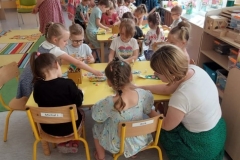 Siedząca grupa dzieci przy żółtym stoliku i wykonująca prace plastyczne.