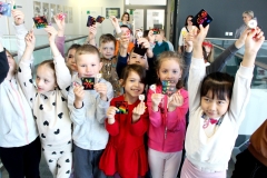 Grupa uśmiechniętych dzieci w wieku przedszkolnym trzymająca w dłoniach kolorowe karteczki.