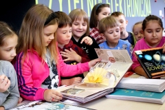 Grupa dzieci przeglądająca z dużym zainteresowaniem książki wyłożone na stoliku.
