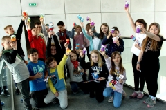 Liczna grupa dzieci prezentuje na wyciągniętych rękach kolorów figurki