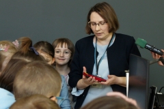 Zastępca dyrektora Biblioteki PB otoczona gromadką dzieci. Stoi obok stanowiska komputerowego przeznaczonego dla osób z niepełnosprawnością.