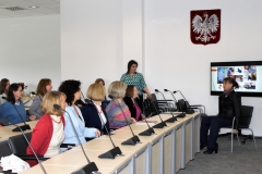 Grupa słuchaczy przygląda się kobiecie siedzącej na krześle.
