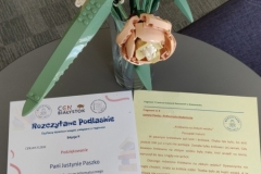 Karta podziękowania Justynie Paszko wraz z treścią czytanki. Obok sztuczne kwiaty.