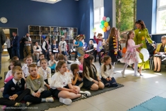 Grupa dzieci siedząca na podłodze. Na drugim planie kilkoro dzieci tańczących wesoło.