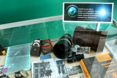 Fragment gabloty, w której leżą duży obiektyw z futerałem, światłomierz, klisze fotograficzne, czarno-białe zdjęcia, książki o białostockich fotografach.
