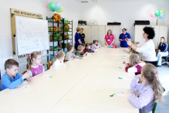 Grupa dzieci uczestniczy w zajęciach przy dużym stole w jasnej sali edukacyjnej.