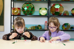 Dwoje dzieci pracuje przy stole z drobnymi materiałami wykorzystywanymi podczas zajęć edukacyjnych