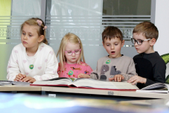 Dzieci siedzą przy stole i korzystają z dużych materiałów edukacyjnych w jasnym pomieszczeniu