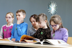 Kilkoro dzieci siedzi obok otwartych książek podczas aktywności edukacyjnej w sali