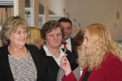 Grupa starszych ludzi słucha oprowadzającej kobiety w czerwonej marynarce, która trzyma w dłoni kartę biblioteczną i pokazuje zebranym.